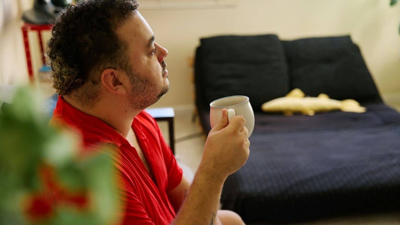 A man in a red shirt holds a coffee mug and looks away from the camera.
