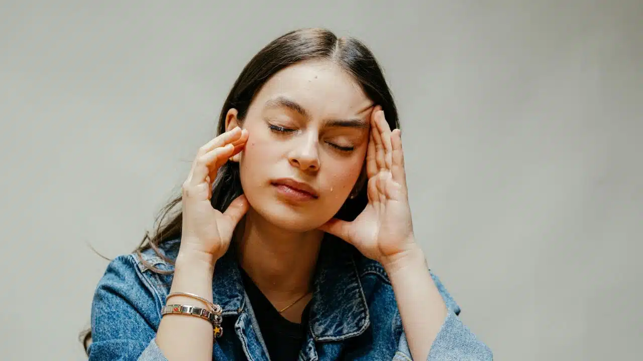 A young woman with long hair holds her temples with her eyes closed.