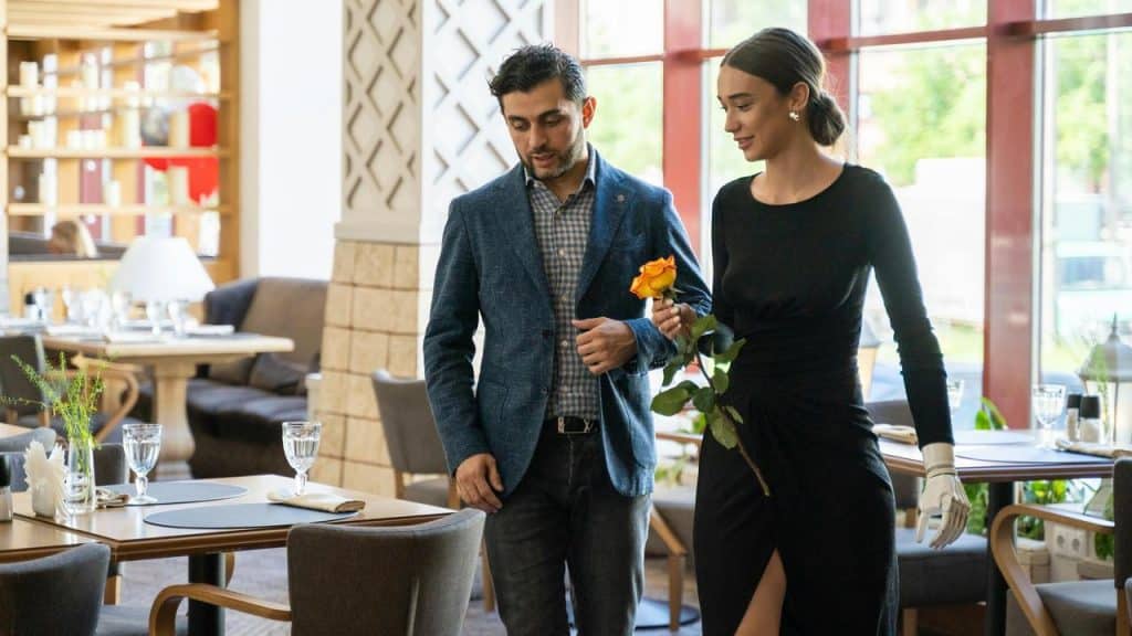 A couple walking into a restaurant, with the man holding a yellow rose for the woman.