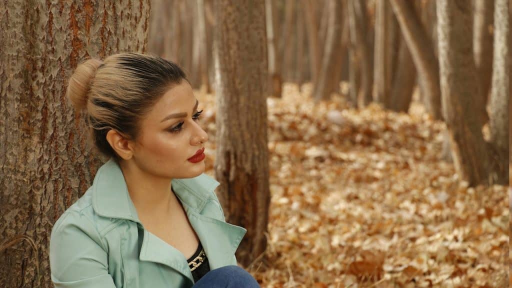 A woman sitting on the ground next to a tree in fall.