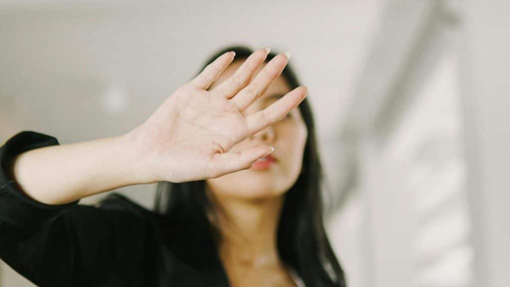 A woman raising her hand to cover her face in a bright indoor setting.