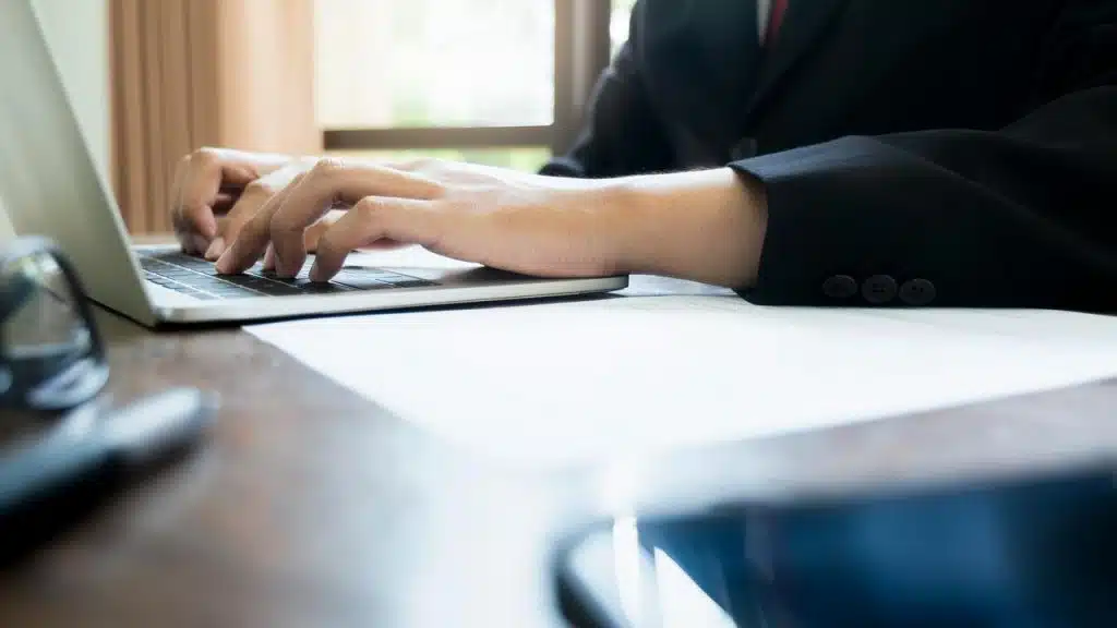 A person in a suit typing on a laptop at a desk.