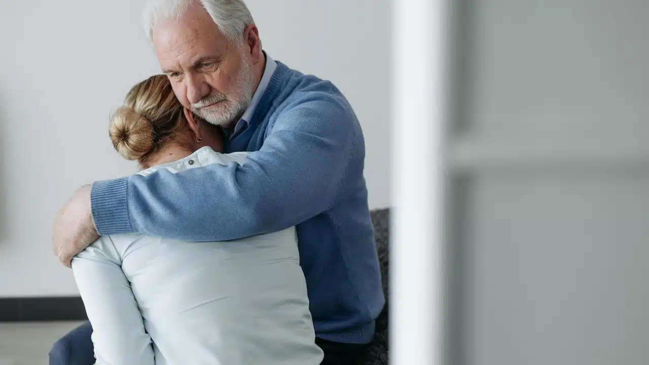 An older man comforting a woman with a hug.