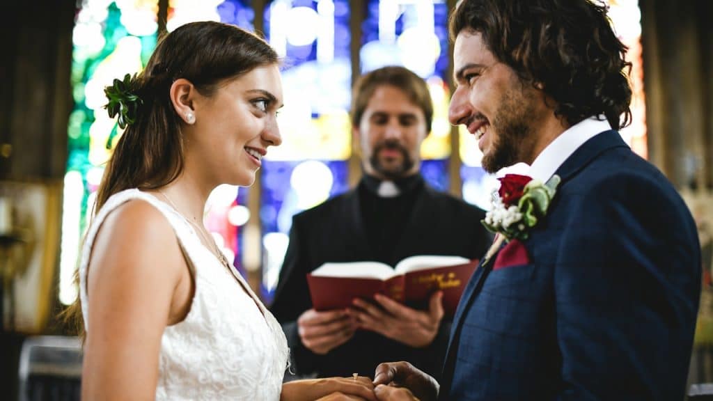A bride and groom at the altar looking into each otherโs eyes.
