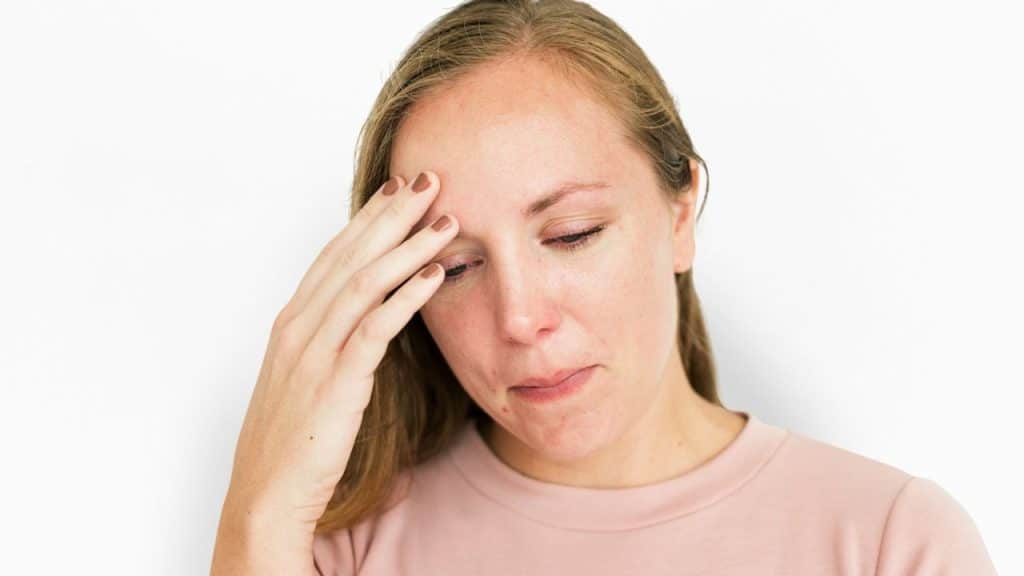 A woman with light brown hair holds her hand to her forehead with a worried expression.