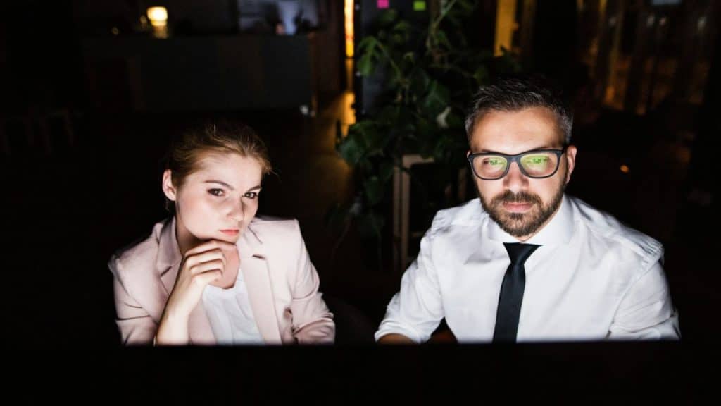 A man  and a woman, sit in a dark office looking intently at a screen.