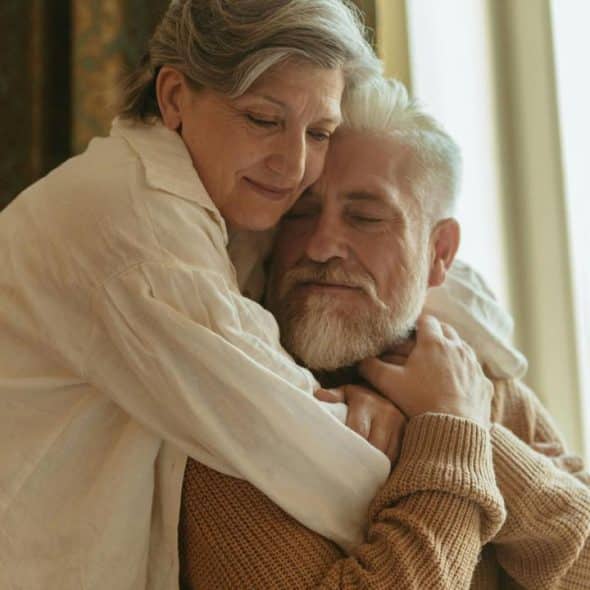 A gentle older couple embracing by a window.