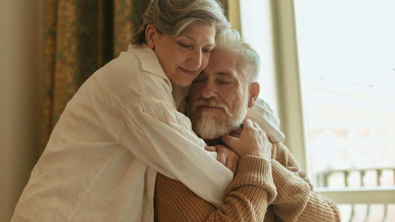 A gentle older couple embracing by a window.