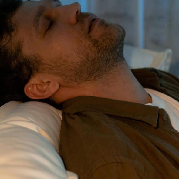 A man resting with his head tilted back on a pillow.