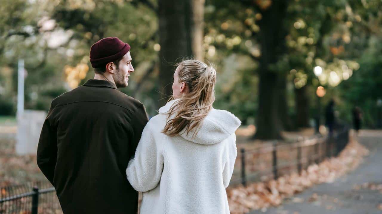 A couple walking together through a park in autumn.