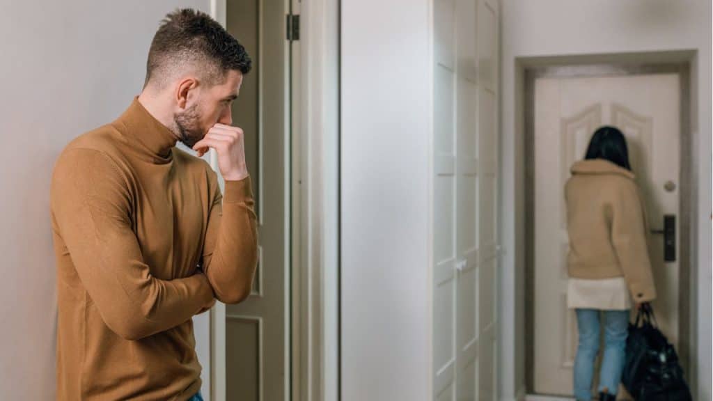 A man watching a woman with a bag leaving through a doorway.