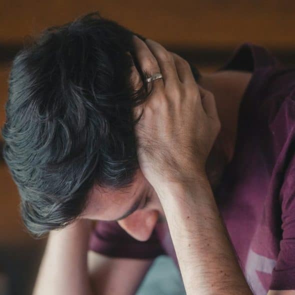 A man in a purple shirt sits with his head in his hands.