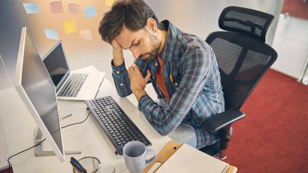 Man sitting at a desk with his head resting on his hand, looking tired.