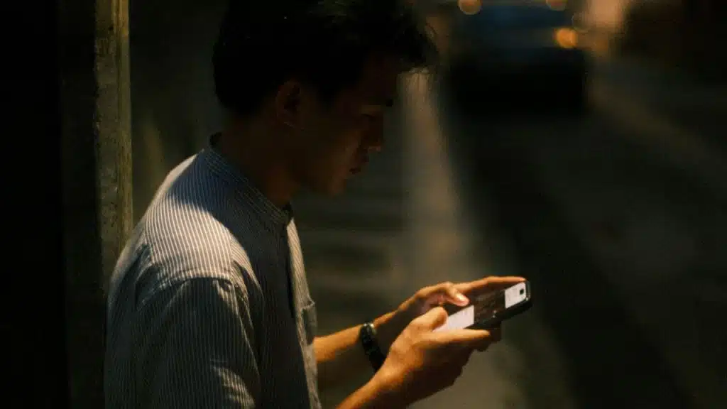 Young man in a striped shirt looking at his smartphone at night.