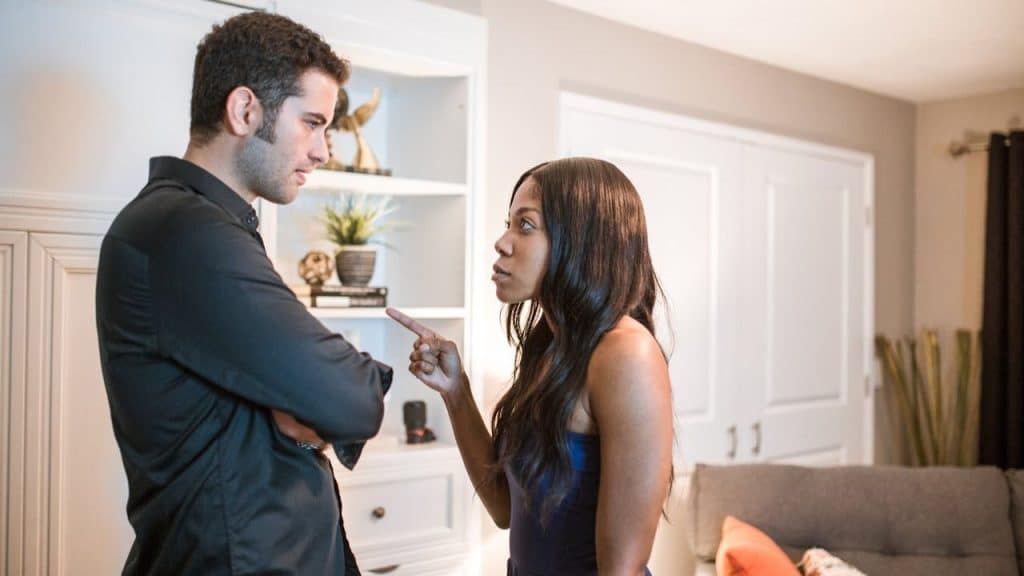 Woman pointing her finger and talking to a man with his arms crossed indoors.