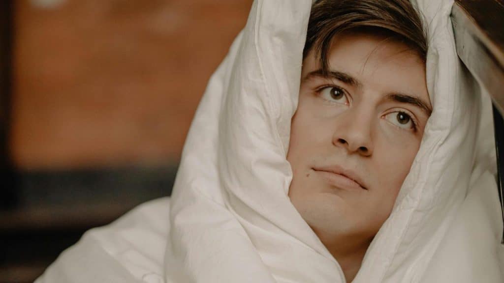A man wrapped in a white blanket looking thoughtful.