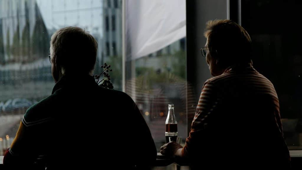 A silhouette of two people sitting by a window with a drink between them.