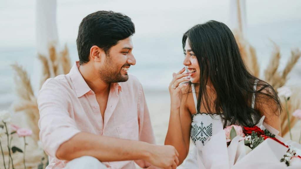 A laughing couple looking at each other outdoors with a bouquet of roses.