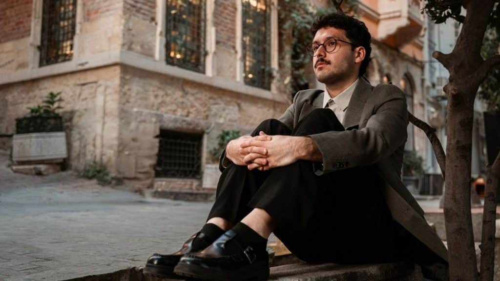 A man in a blazer and glasses sitting on a step outside a brick building.