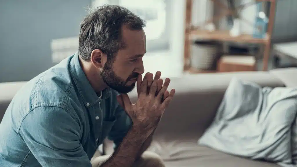 A bearded sitting on a couch and looking anxious.