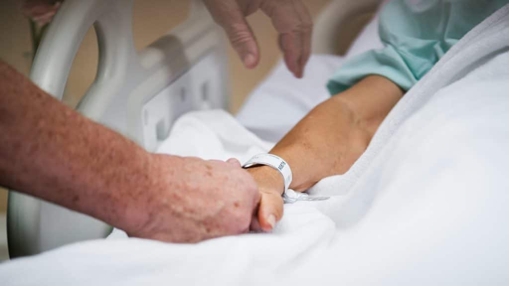 An older couple holding hands in the hospital bed.