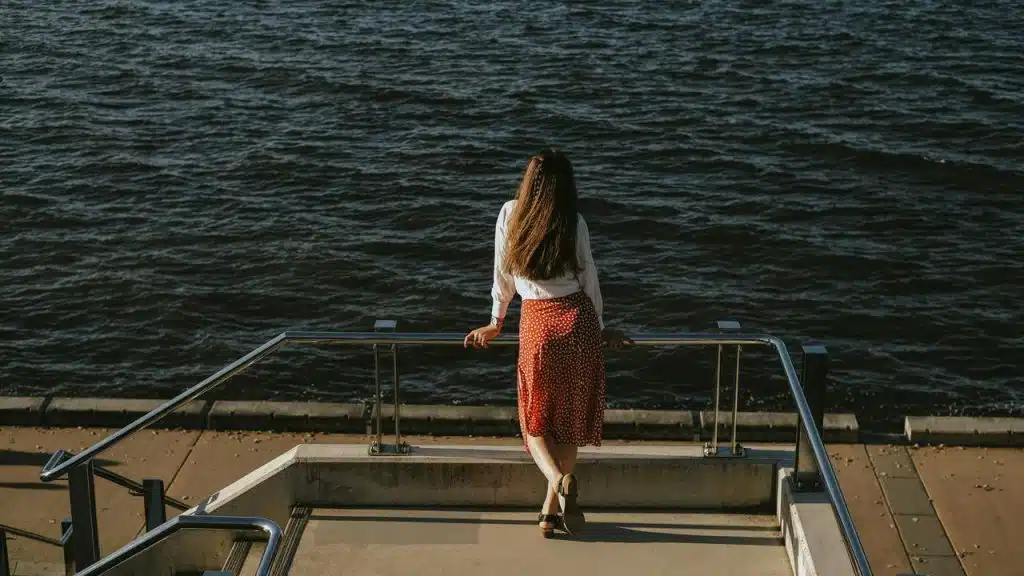 A woman standing by a waterfront railing, looking out at the water.