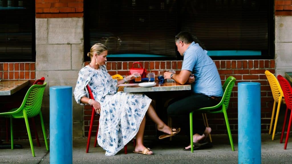 A man and woman sit facing each other at an outdoor cafe table.