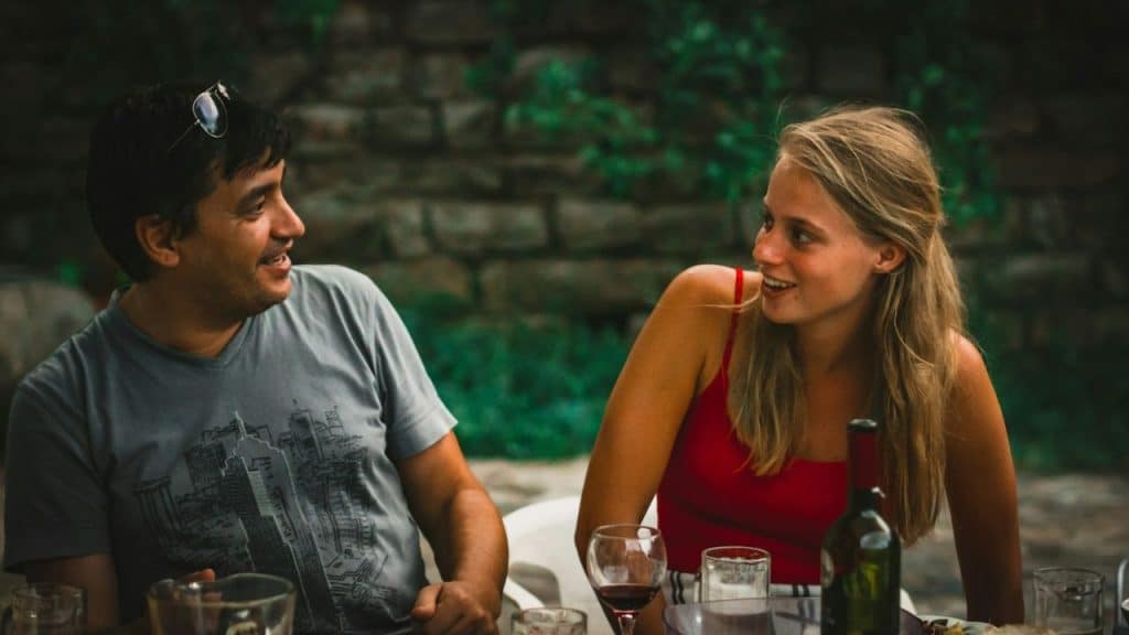 Smiling man and woman talking to each other at a table with wine glasses outdoors.