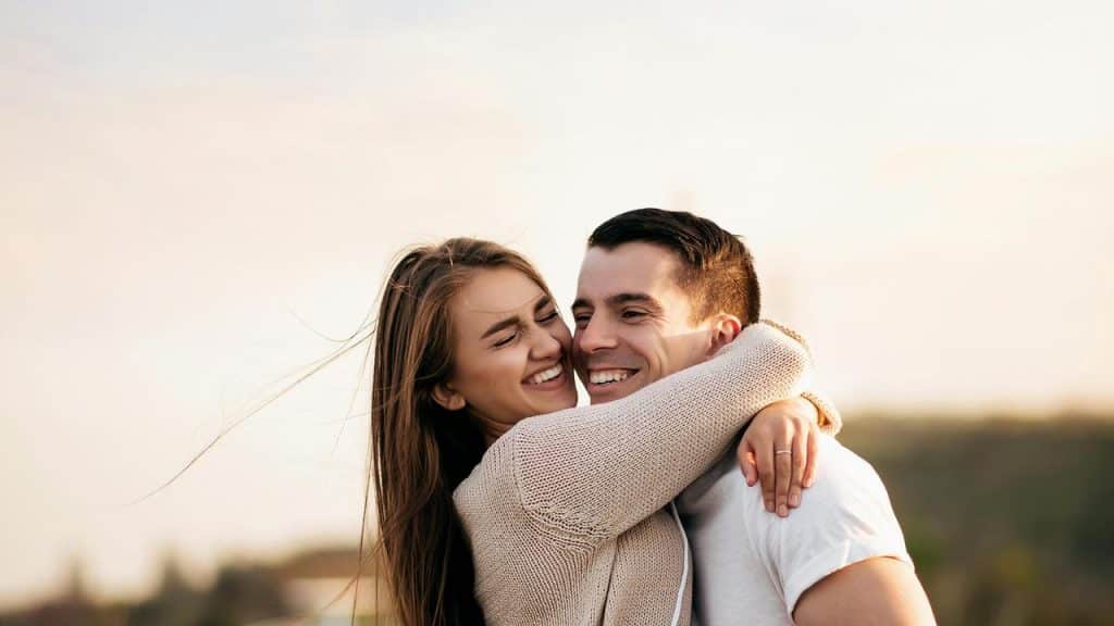 A woman embracing a smiling man during a moment outdoors.