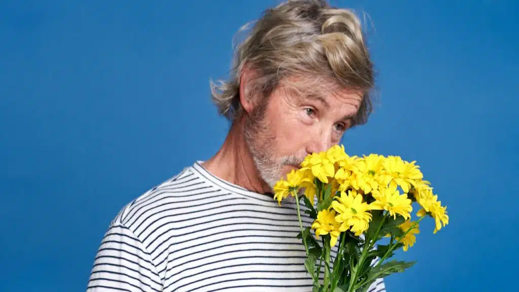 An elderly man holding a bunch of yellow flowers.