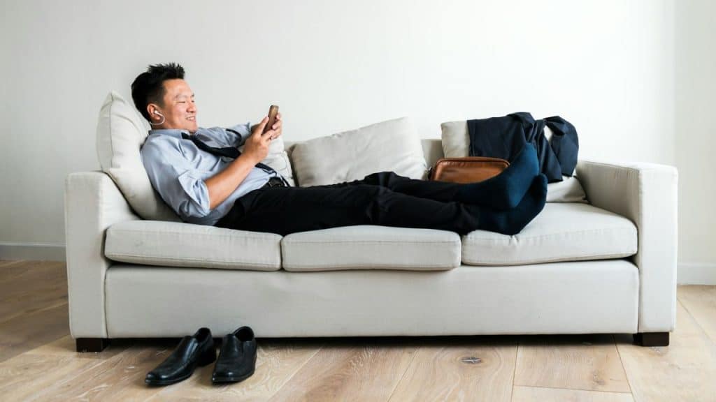 Man in business attire relaxing on a white couch, looking at his phone.