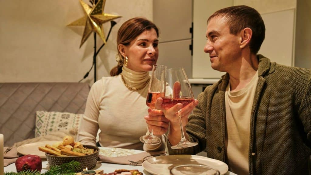 Man and woman at a dinner table toasting with glasses of rose-colored wine.