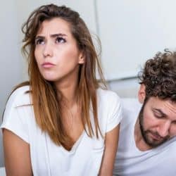Woman looking up with a worried expression, sitting next to a man looking down.