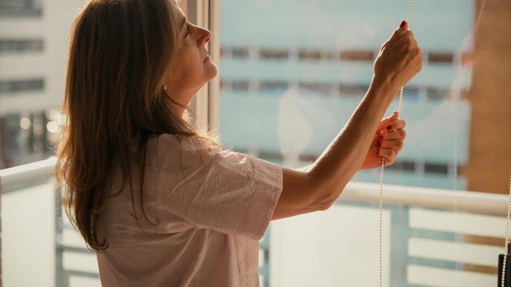 A person raises window blinds in warm sunlight.