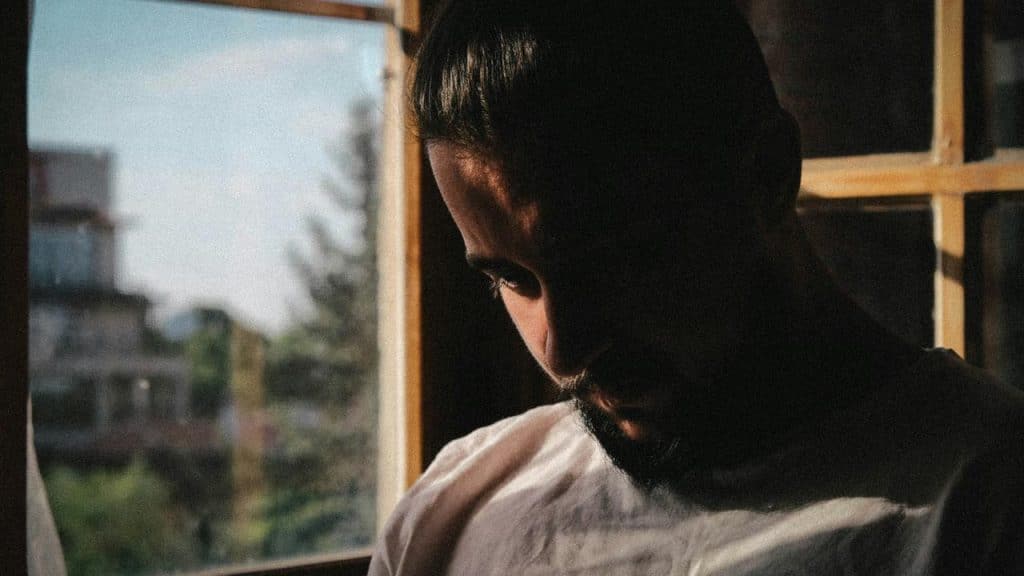 A man sitting by a window with his head bowed in soft sunlight.