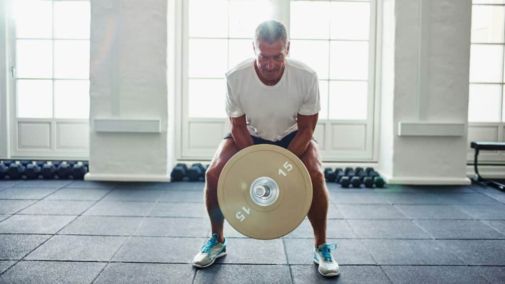Middle-aged man in a white shirt performing a squat with a single weight plate.