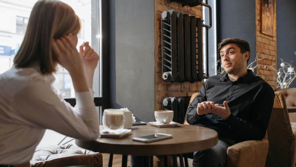 A man and woman sitting in a cafรฉ having a conversation over coffee.
