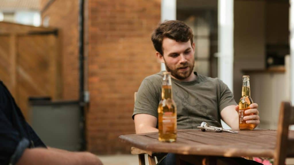 A man sitting at a table holding a beer bottle with another bottle in front of him.
