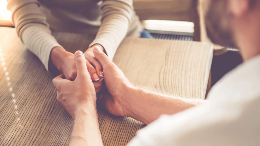 Close-up of a couple holding hands across a wooden table.