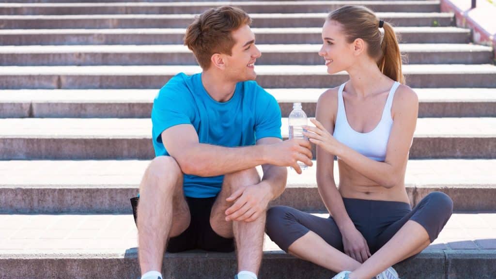 Smiling fitness couple taking a break and sitting on outdoor steps.