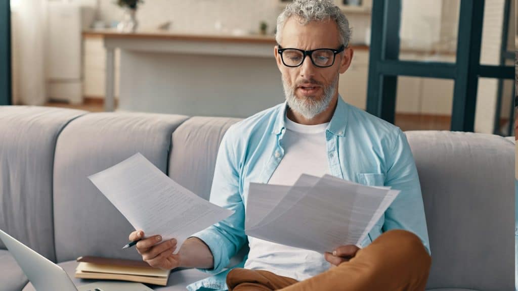 A man reading financial papers while sitting on a table.