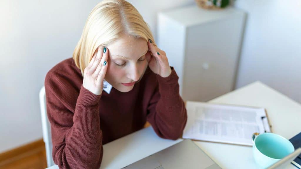 A woman sitting at a desk holding her temples as if stressed or tired.