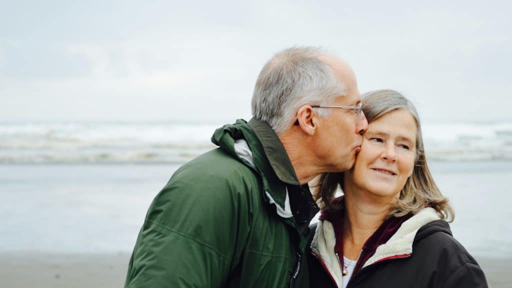 A man kissing his wife beside a body of water.