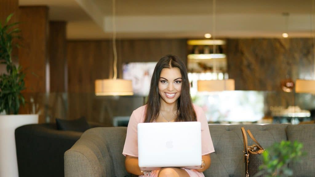 A woman smiling and using a laptop while sitting on a couch in an office.