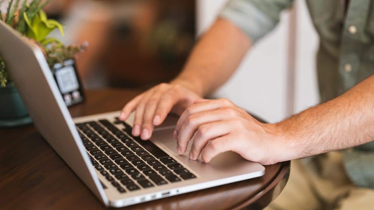 A person typing on a laptop at a wooden table.