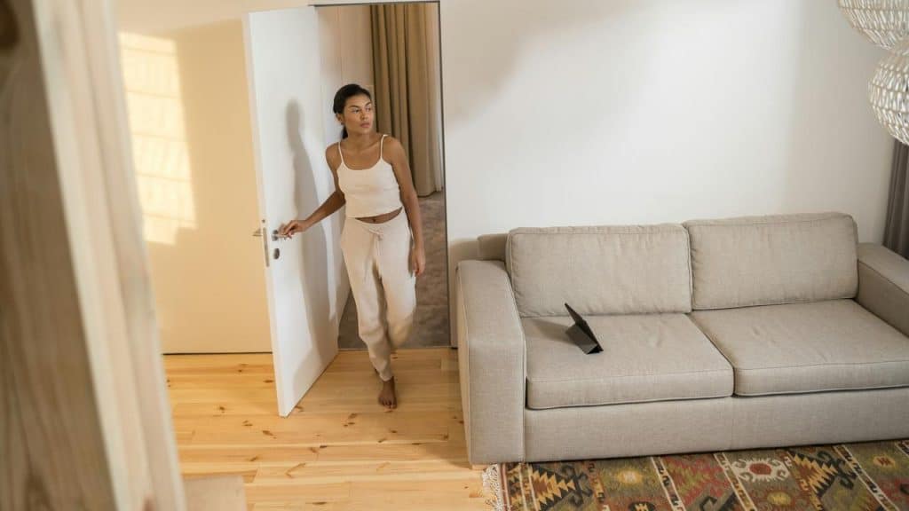 A woman in loungewear enters a bright living room with a beige couch.