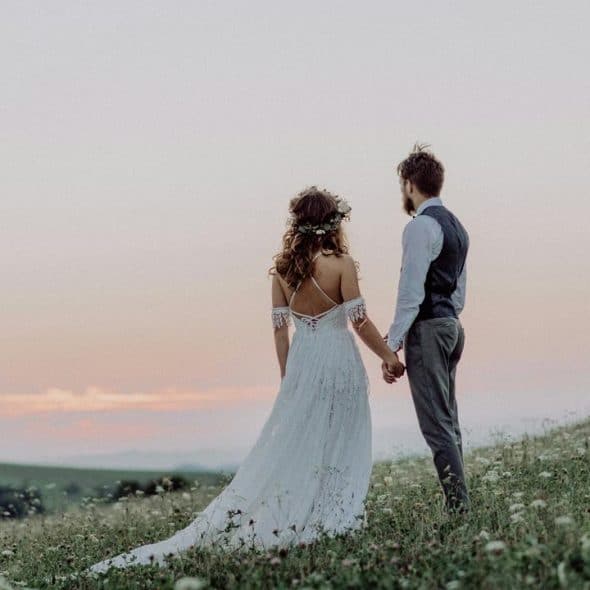 A bride and groom holding hands in a grassy field at sunset.