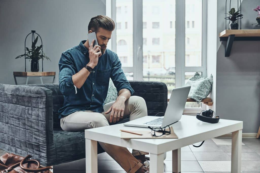 A man talking to someone on his phone while sitting in front of a laptop.