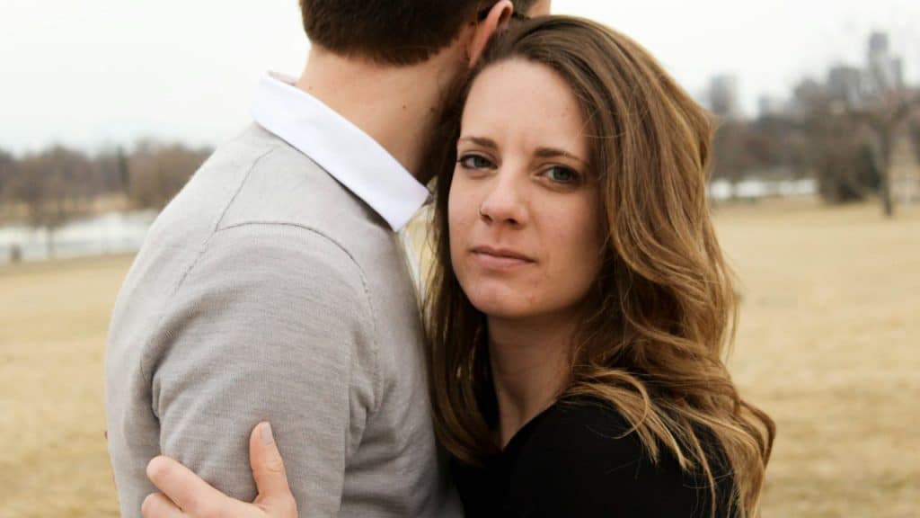 A woman hugging a man and looking concerned while they stand outdoors.