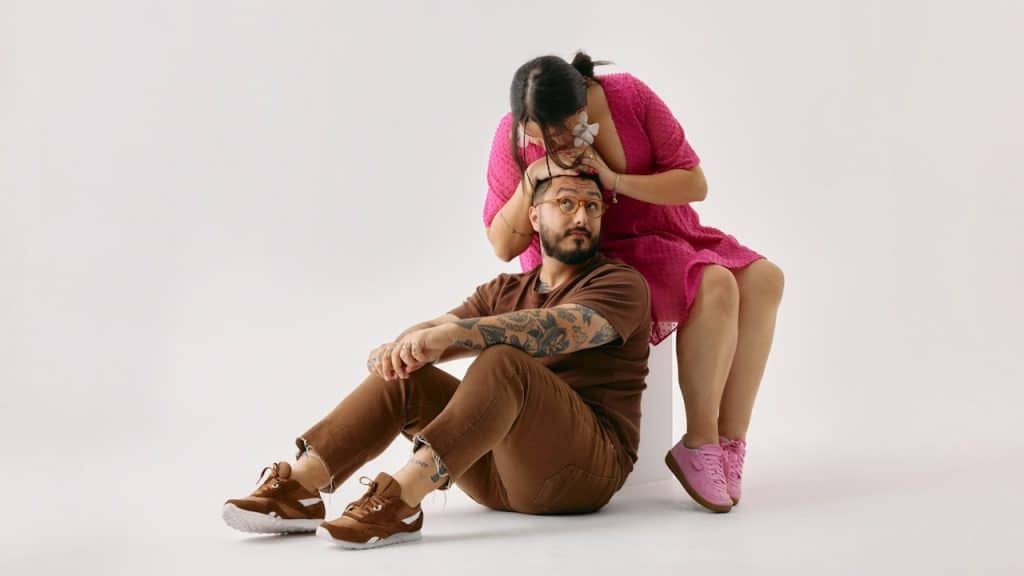A woman holding her husband’s head who is sitting on the floor next to her.